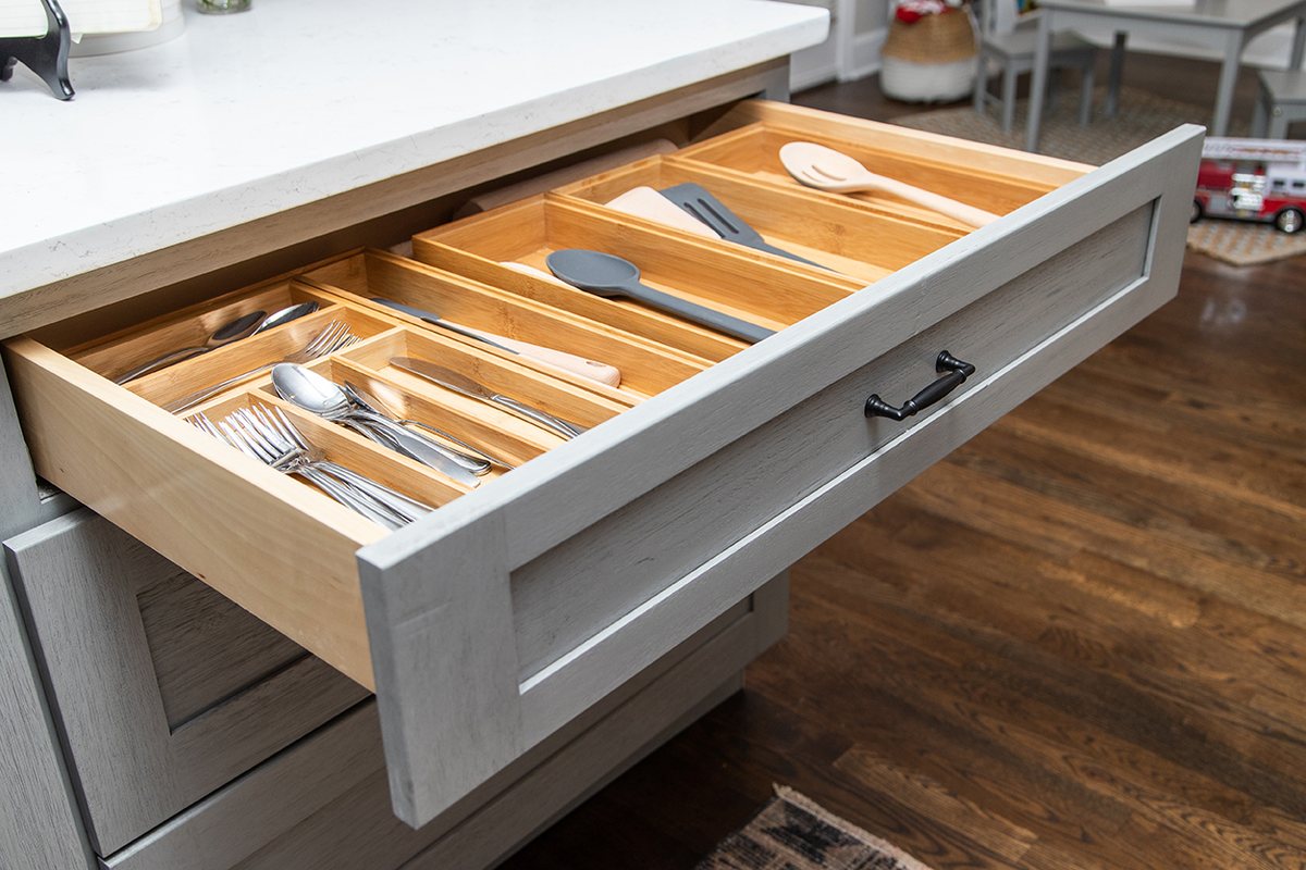 A full-extension drawer pulled open with a wood utensil organizer, in Nova Light Gray