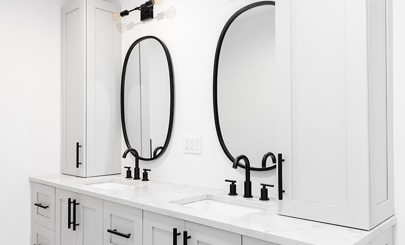 White bathroom vanity with black hardware and slim wall cabinets on either side.
