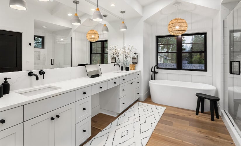 Large bathroom with long white cabinets, white countertop, and large soaker tub underneath window.
