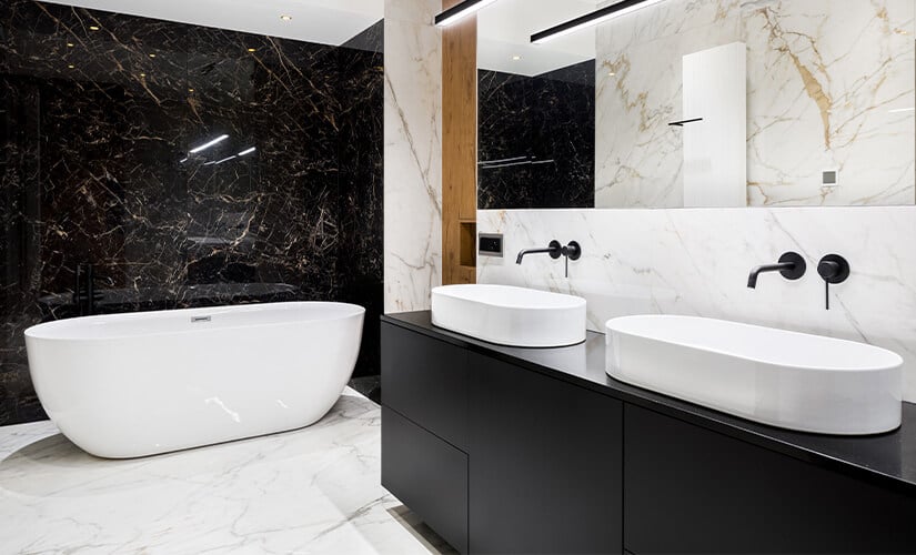 Bathroom with black vanity and accent wall and white sinks and soaker tub.