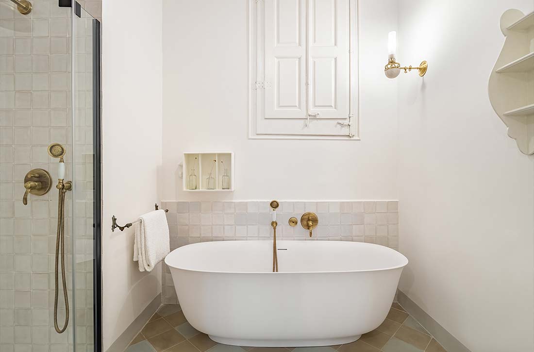 White bathroom with vintage freestanding tub abd brass candlestick sconce.