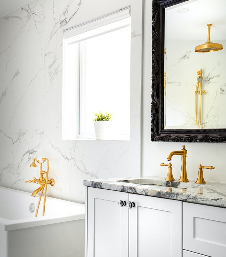 Glamorous bathroom with matching gold fixtures for sink and bathtub.