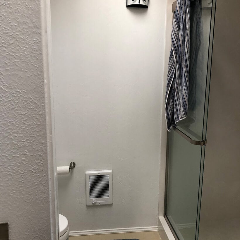 Tight and dark bathroom with shower and toilet behind wall.