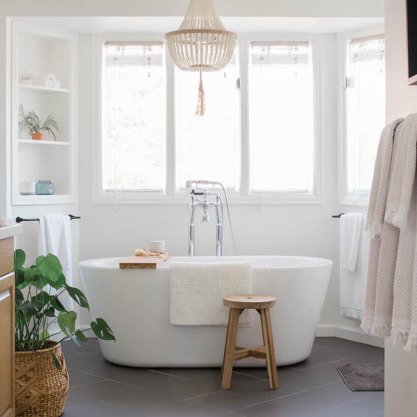Freestanding white soaker tub under large window in newly renovated, modern bathroom.