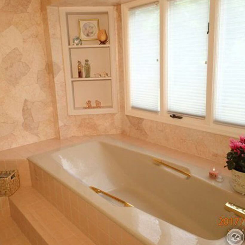 Outdated pink bathroom with inset bathtub under window.