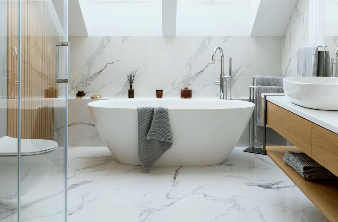 Bathroom with marble floors and walls and white bathtub.