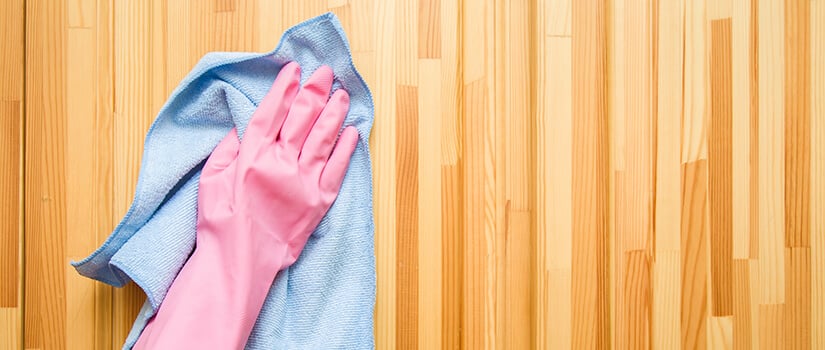 Person with a glove on cleaning wood kitchen cabinets