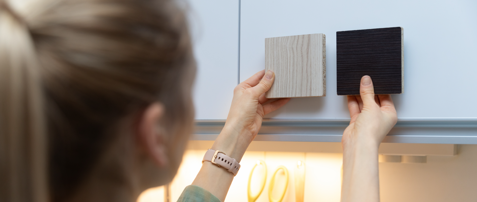 Woman comparing kitchen cabinets samples against white cabinets.