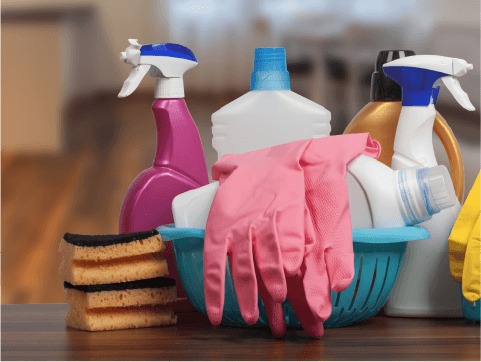Gloves, sponges, and bottles of cleaning spray on a wooden countertop.