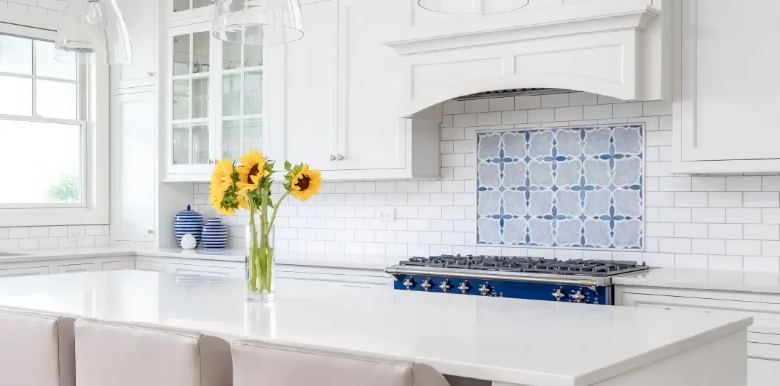 Light coastal island kitchen with white subway tile backsplash, blue tile accents over the stove, and traditional white cabinets.