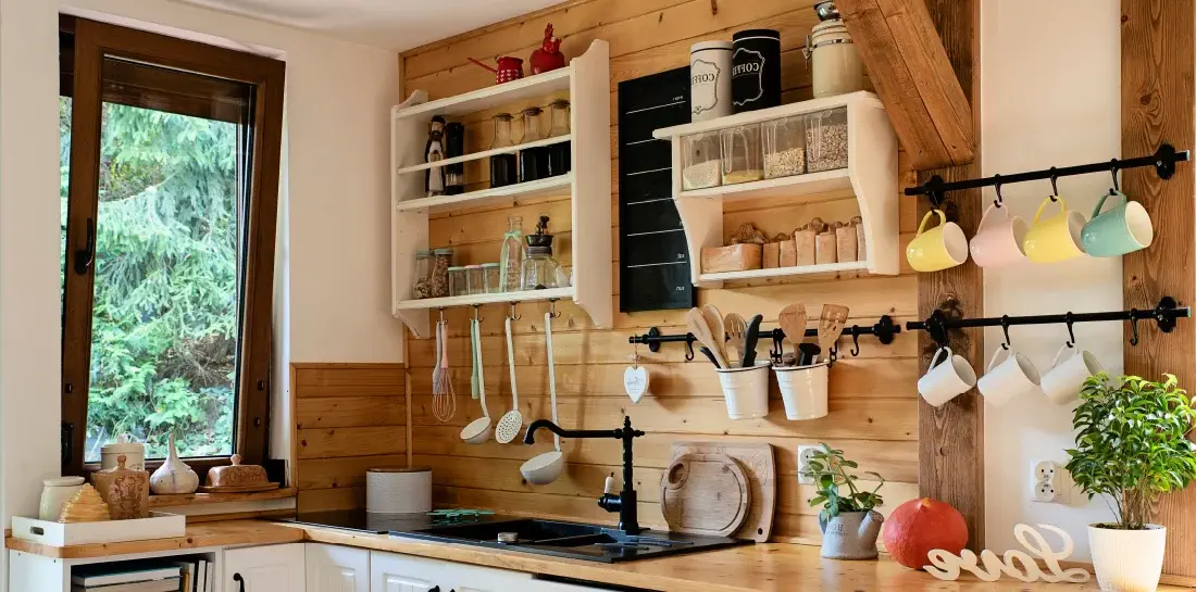 Homely kitchen sink with shiplap wall and a variety of utensils placed on open shelving.