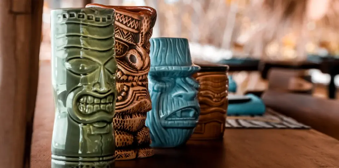Four tiki-style bar glasses placed on a wood countertop.