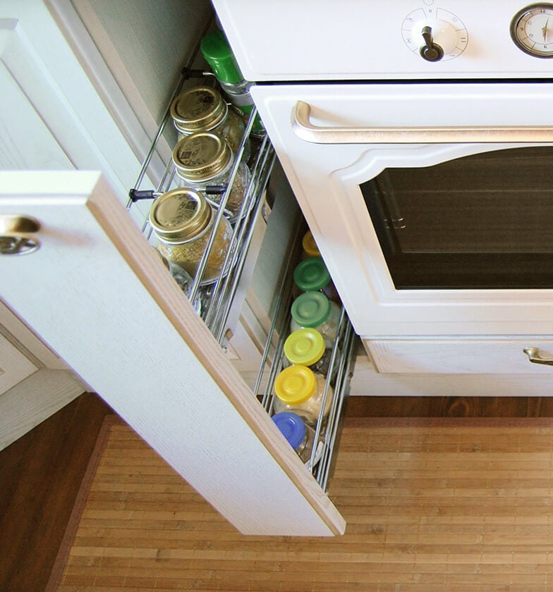 White narrow pullout cabinet drawer with spices and jars on racks.