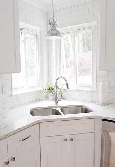 Double basin stainless steel corner sink in white kitchen.