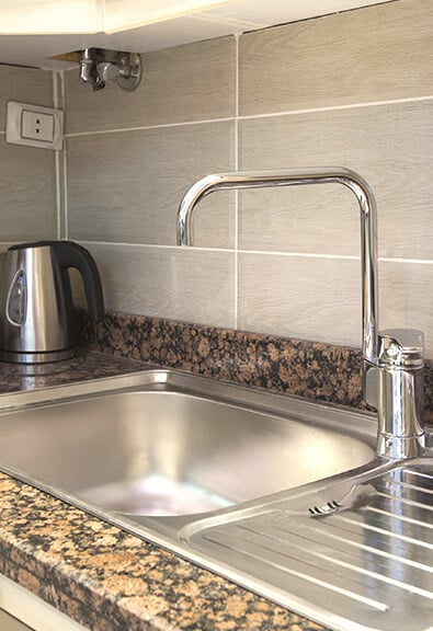 Stainless steel corner kitchen sink with drainboard on granite counters.