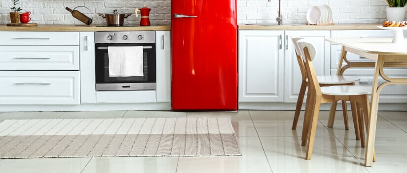 Light kitchen with tan countertop and white cabinets, red retro refrigerator, and textured rug on the floor.