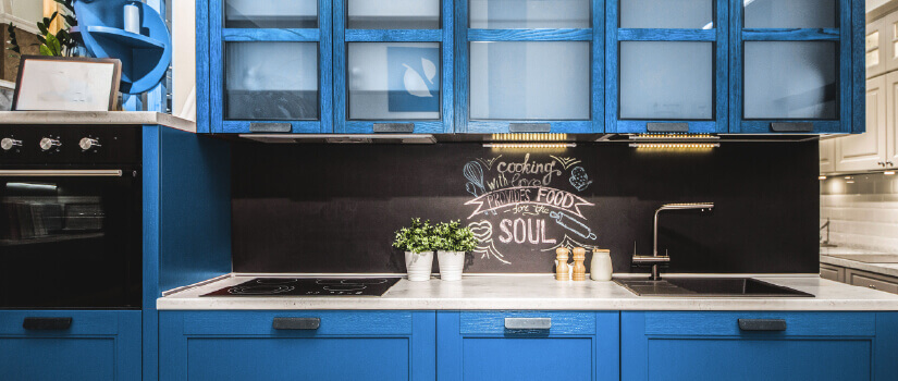 Kitchen with blue cabinets, white countertop, and blackboard-style backsplash with drawing.
