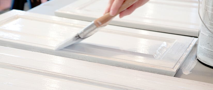 Close up of woman painting kitchen cabinet doors white.