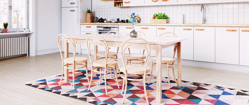 One-wall kitchen with white cabinets, wood countertops, and light wood dining table placed on colorful geometric rug.