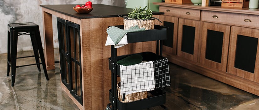 Kitchen towels and houseplant placed on black bar cart placed against the side of a wood kitchen island with black countertops.