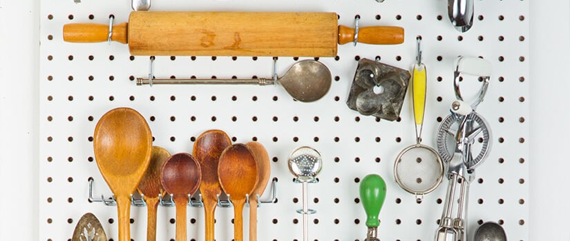 Rolling pin, wooden spoons, and miscellaneous kitchen gadgets hung on white pegboard.