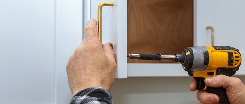 Close up of man screwing gold handles onto white kitchen cabinet.