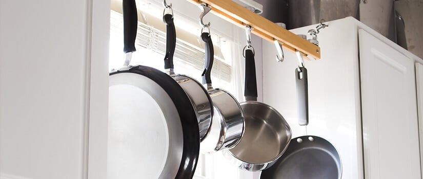 Five pots and pans hanging on rack installed in front of kitchen window.