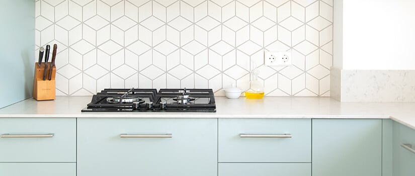 Kitchen with powder blue cabinets, white countertops, and white and gray wallpaper backsplash with a geometric pattern.