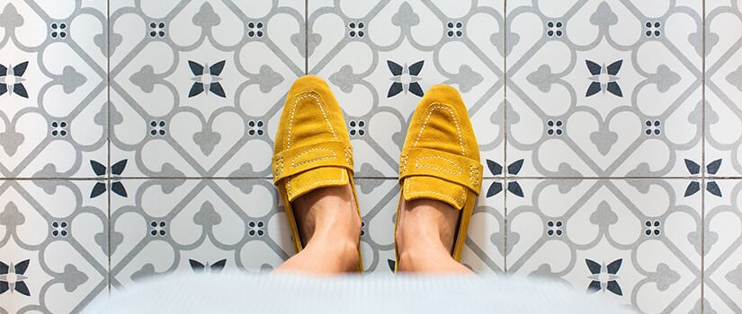 Woman in yellow loafers standing on kitchen floor covered in gray and blue patterned peel-and-stick tiles.