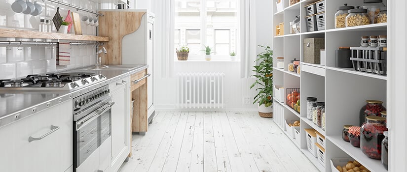 White galley kitchen with stainless steel countertops and wall-to-ceiling built-in kitchen shelving on right wall.