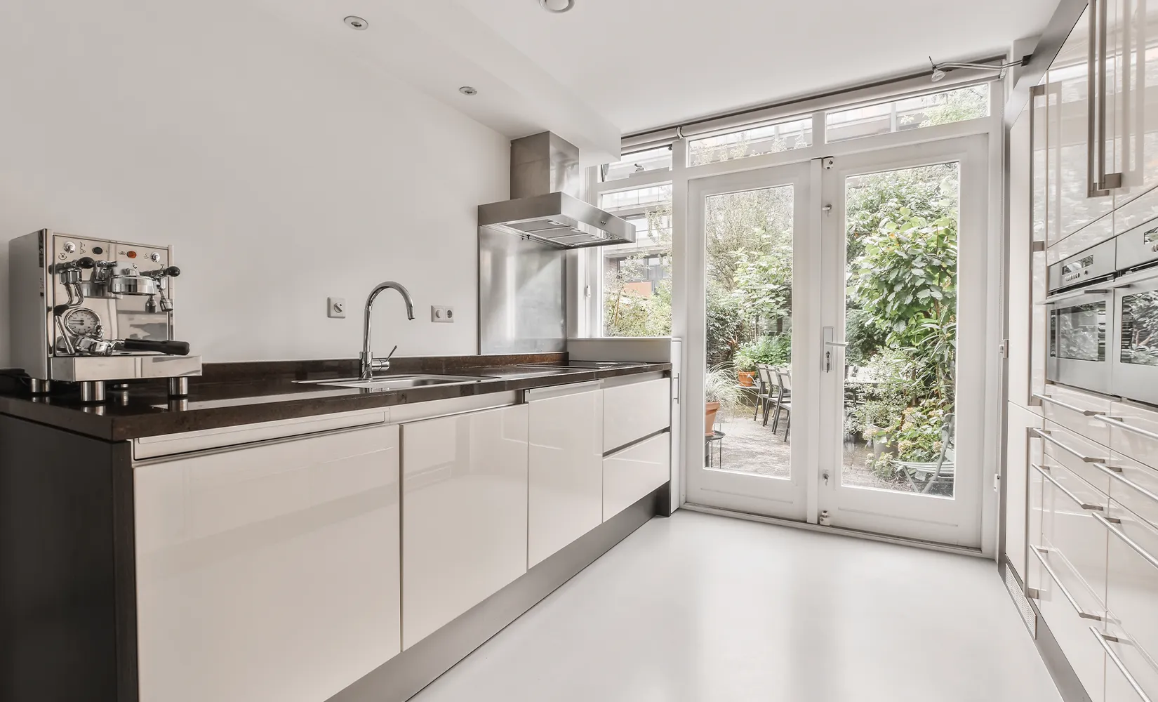 Galley kitchen with white gloss slab cabinets, black countertops and stainless stell appliances.