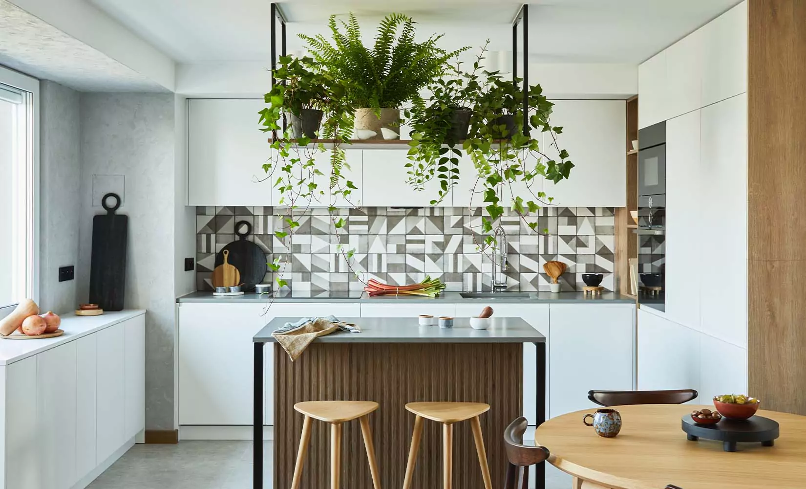 White kitchen with gray geometric backsplash and live plants.