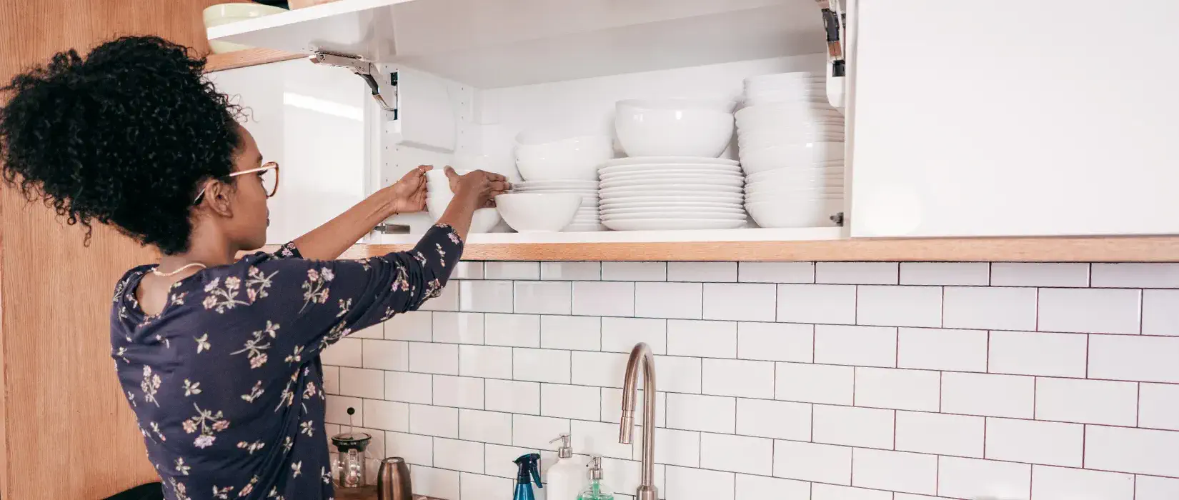 A woman organizing kitchen cabinets with dishware.