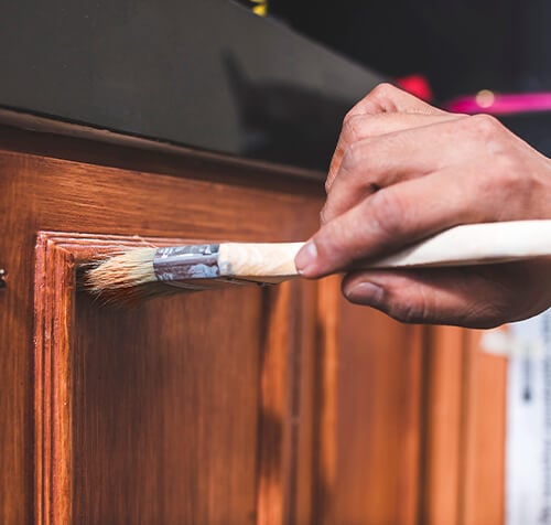 Person using paint brush to apply varnish and protect their painted kitchen cabinets.