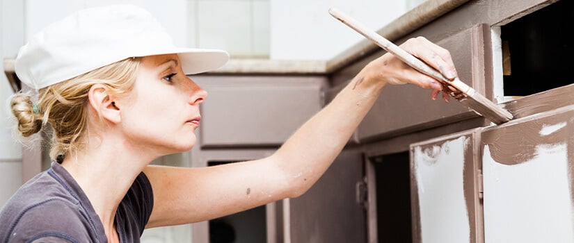 Woman painting kitchen cabinets.
