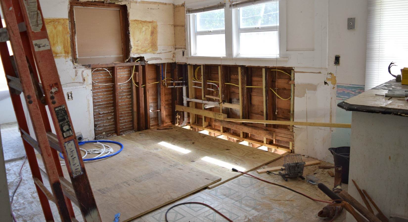 Kitchen in the middle of renovation with open walls containing wires and pipes.