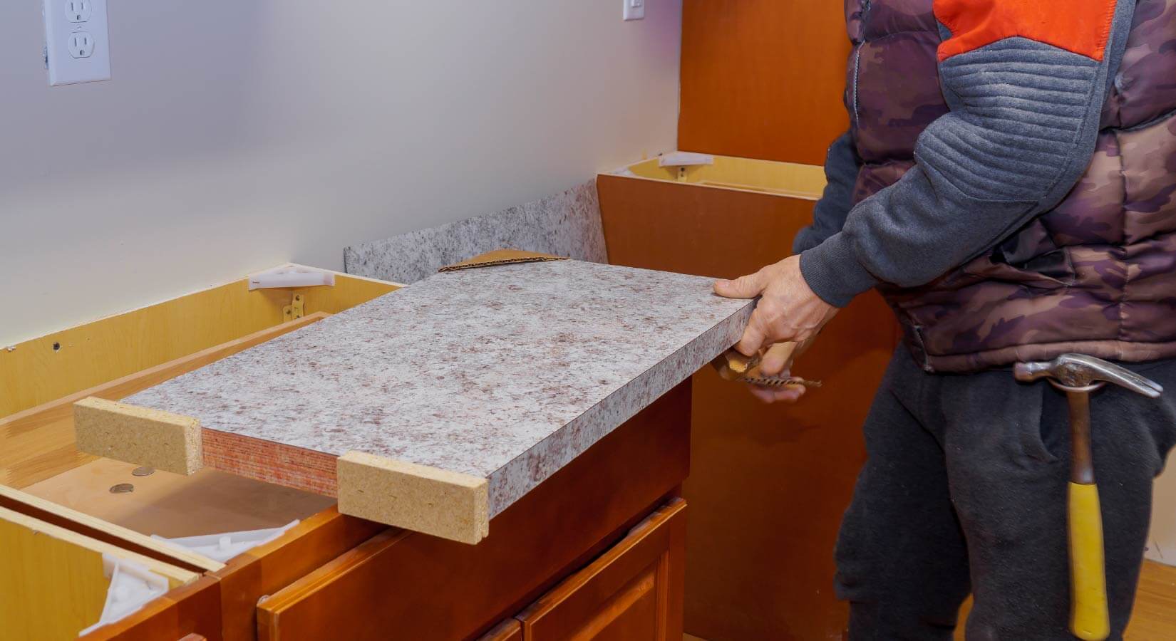 Person aligning faux gray granite countertops on top of warm oak cabinets.