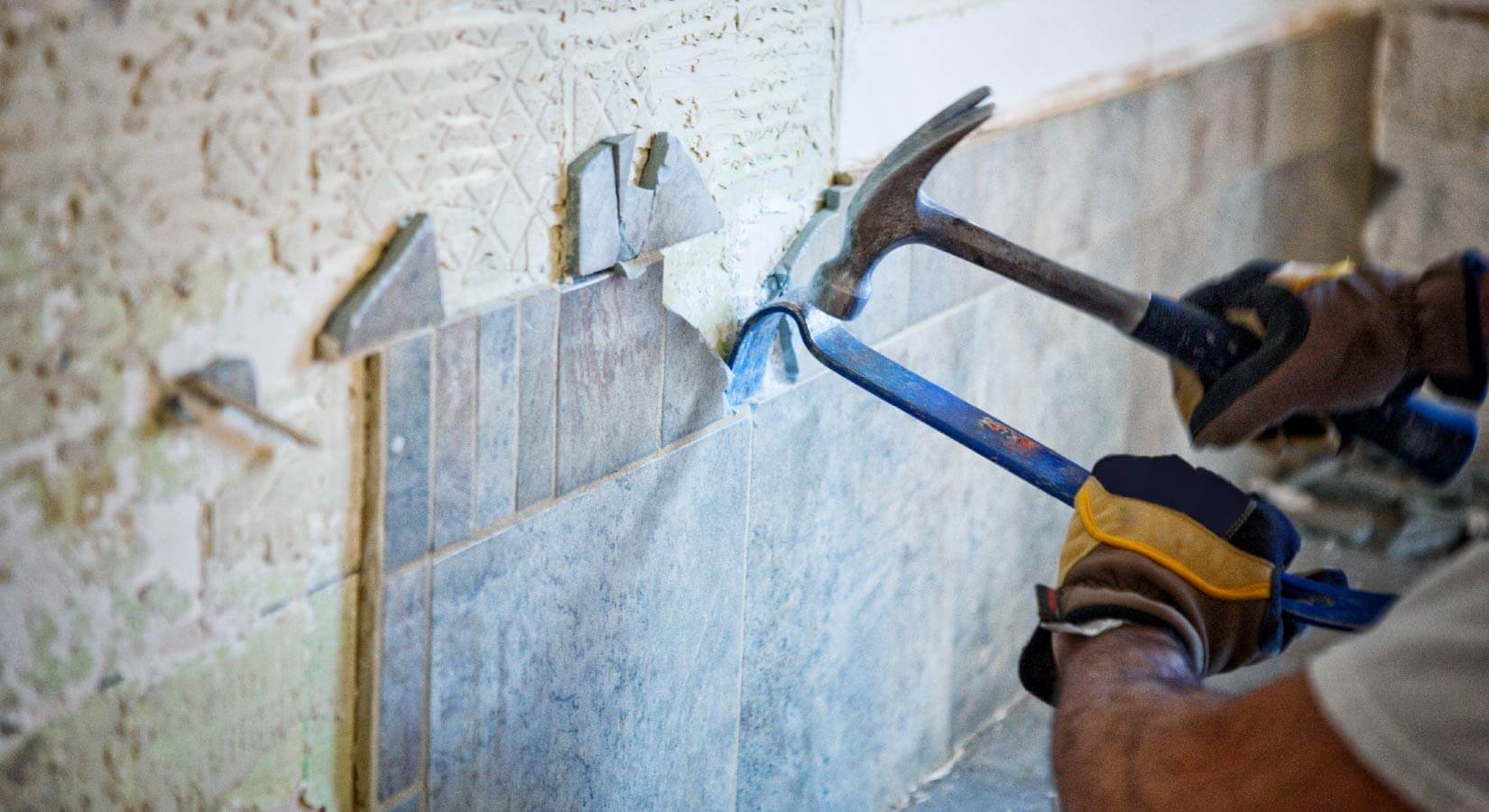 Man removing blue tile backsplash from kitchen wall with crowbar and hammer.