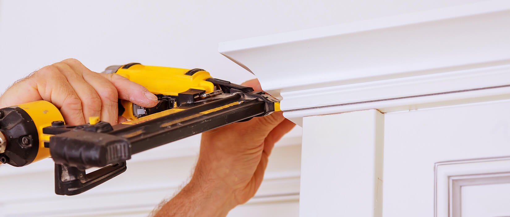 Close-up of a person installing trim to top of upper kitchen cabinets.