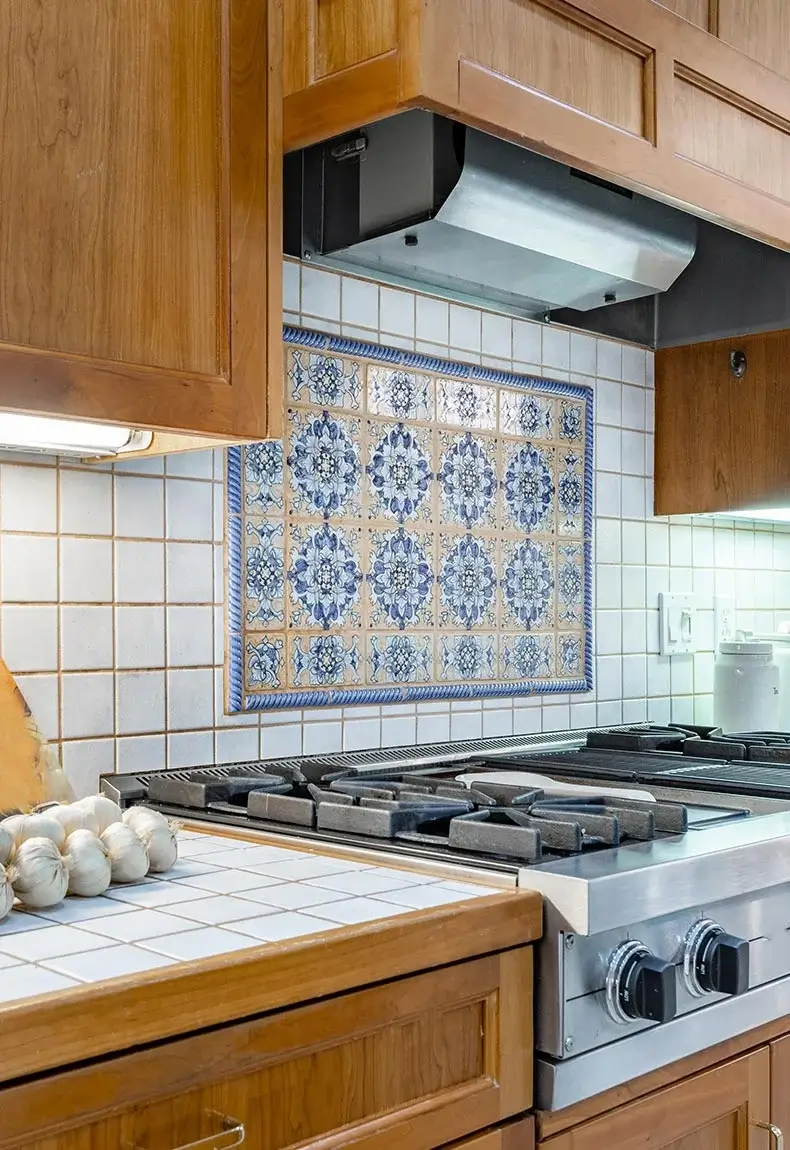 Classic kitchen with gas stove, brown cabinets, and mosaic antique tile backsplash against square subway tile wall.