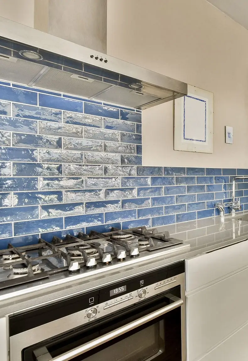 Modern kitchen with white cupboards and blue and white tile backsplash with gas stove oven in the middle.