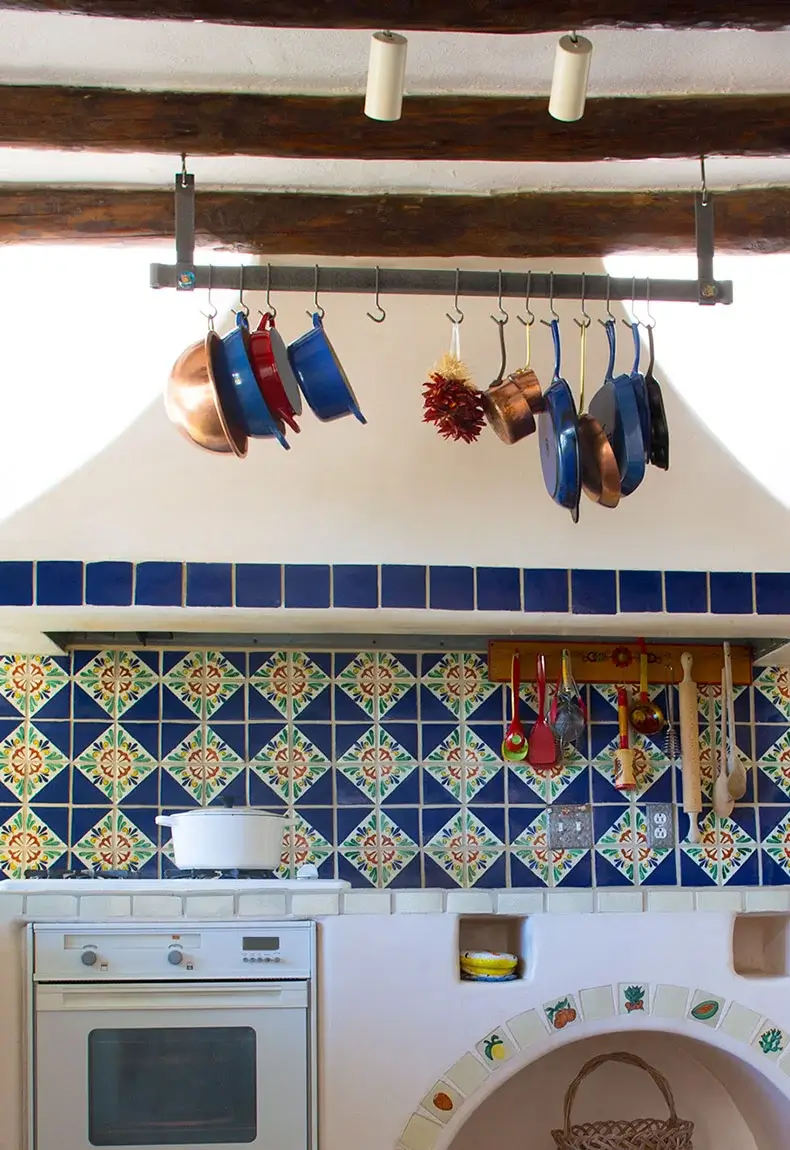 Mediterranean-style kitchen backsplash with blue and green textile patterns and hanging kitchen accessories.