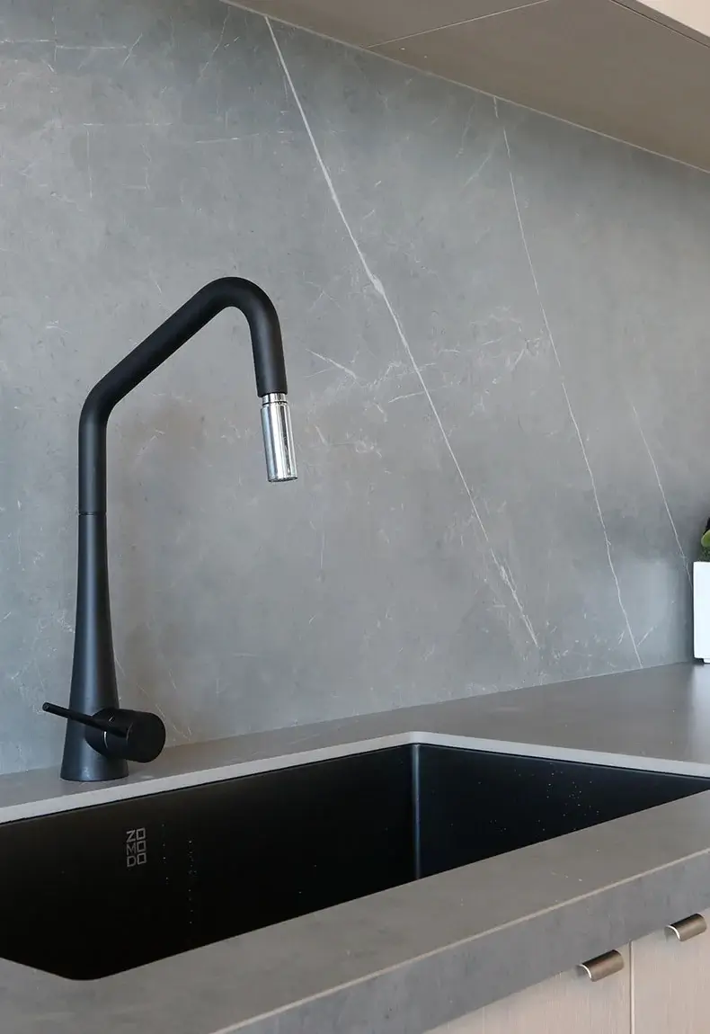 Kitchen with gray concrete slab backsplash and black faucet.