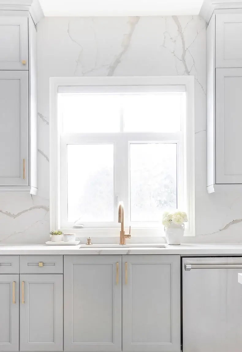 White kitchen with open windows and marble slab backsplash.