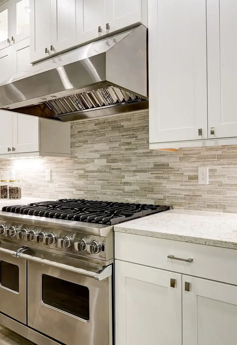 Elegant kitchen with gas stove, marble countertops, and white and gray faux stone backsplash.
