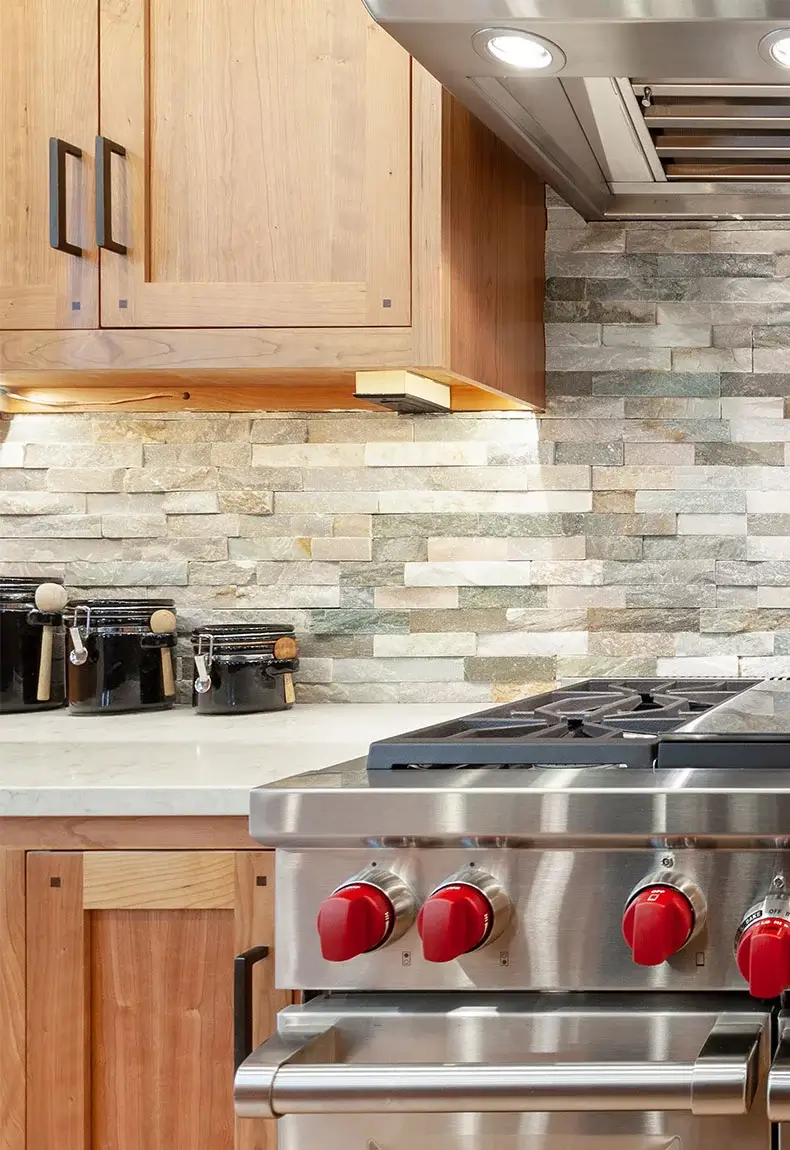 Kitchen with stainless steel oven and a slate stone backsplash with green, blue, and red color hues.