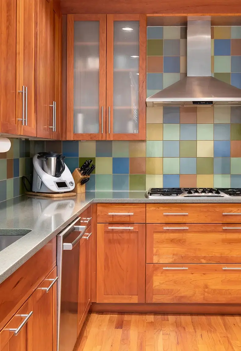 Kitchen with wood cabinets, gray countertops,kitchen appliances, and colorful square tile backsplash.