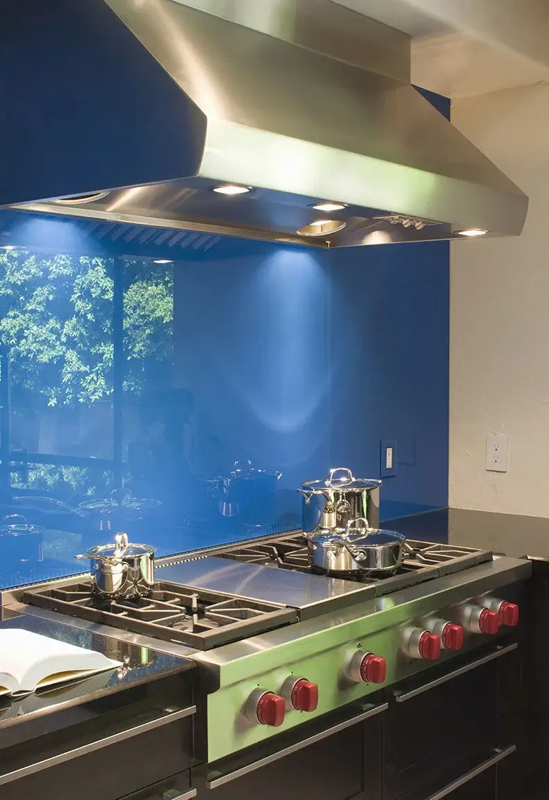 Kitchen with black countertops and drawers, a stove top with red knobs, and a shiny blue reflective backsplash.