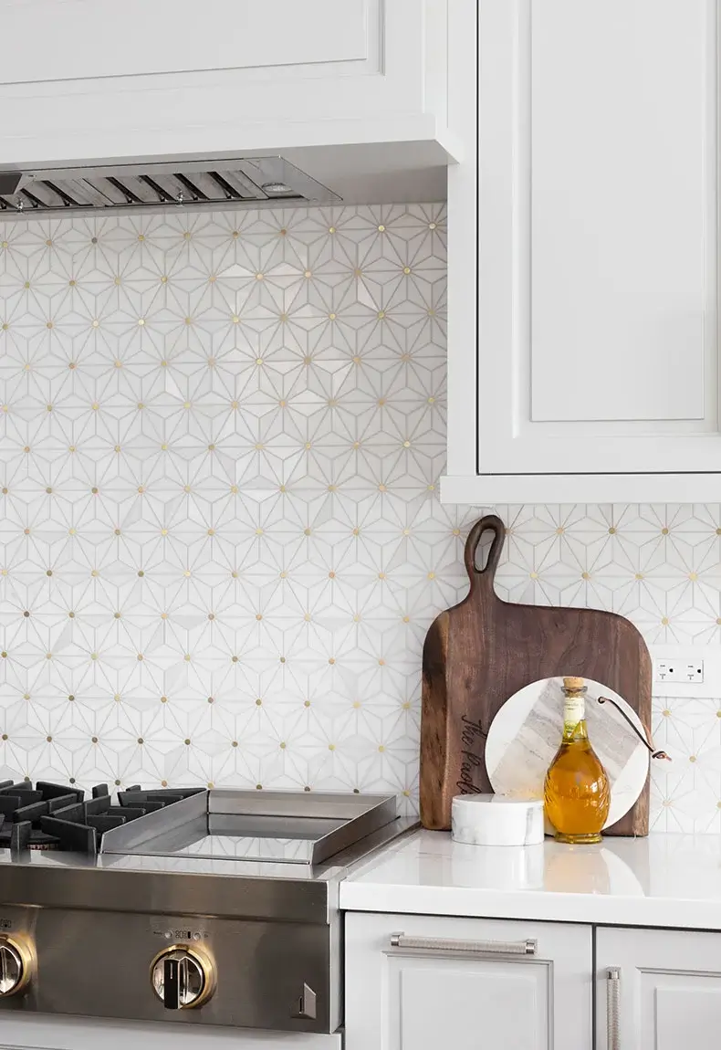 Modern kitchen with white counters, oven with gold knobs, and white and gold tile backsplash with unique abstract patterns.