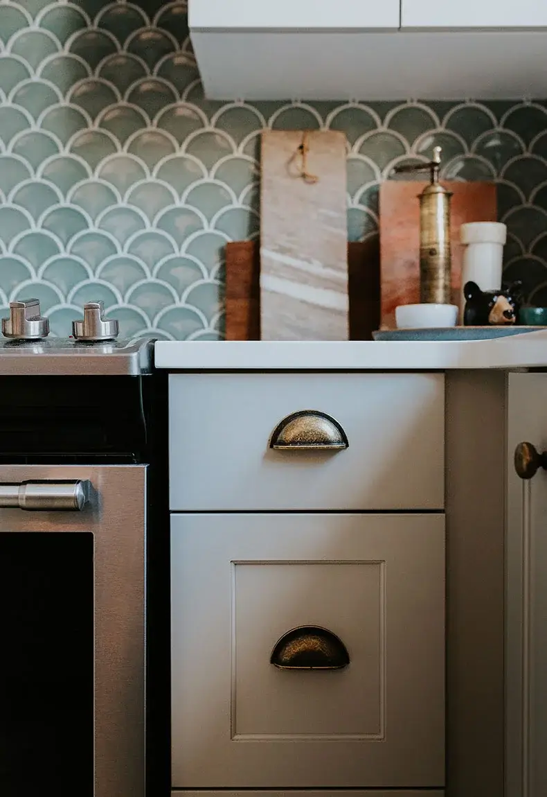 Vintage kitchen with white drawers, rustic kitchen appliances, and fish scale inspired teal and white kitchen backsplash.